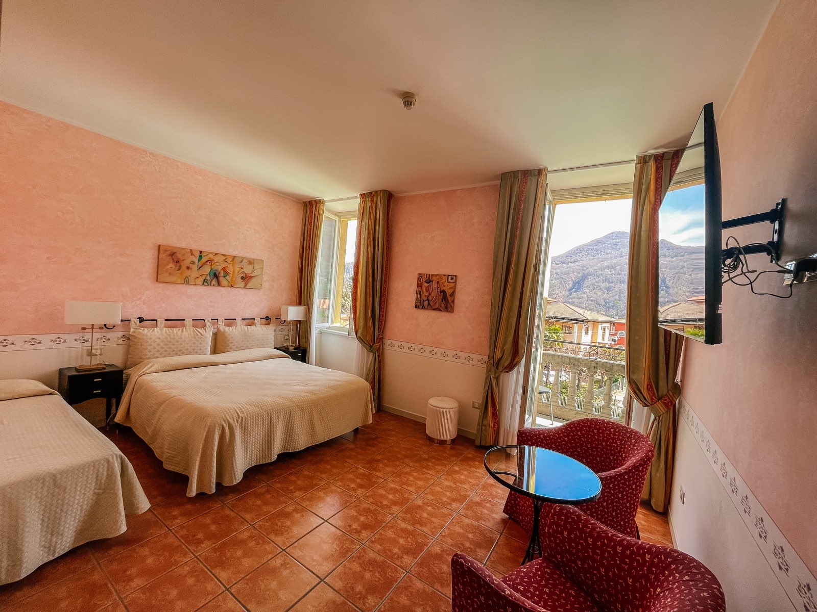 Family Room: a pink room with a double and a single bed, red armchairs and a window to the mountain.