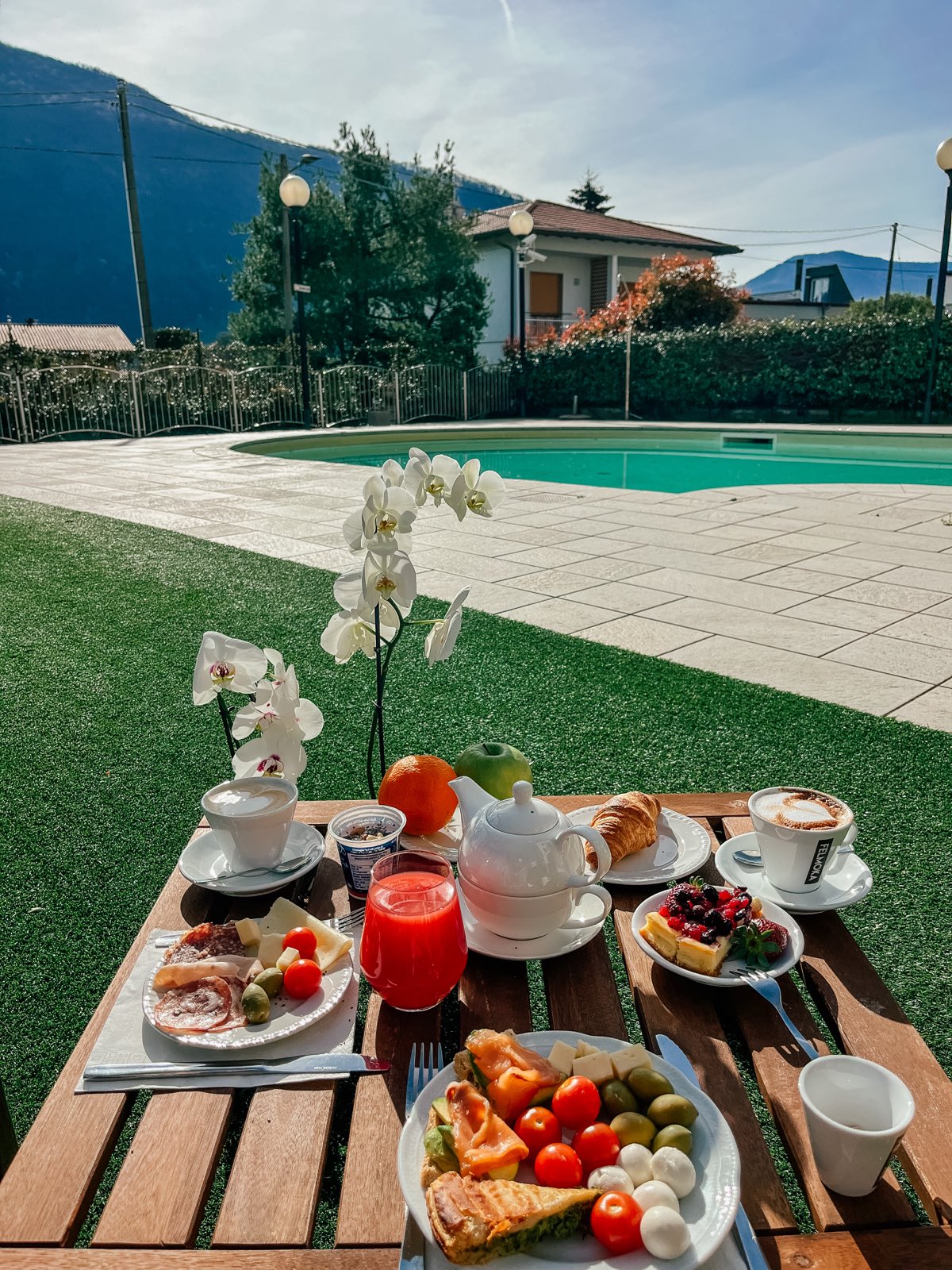 A breakfast table on the lawn by the pool, orchids and mountains.