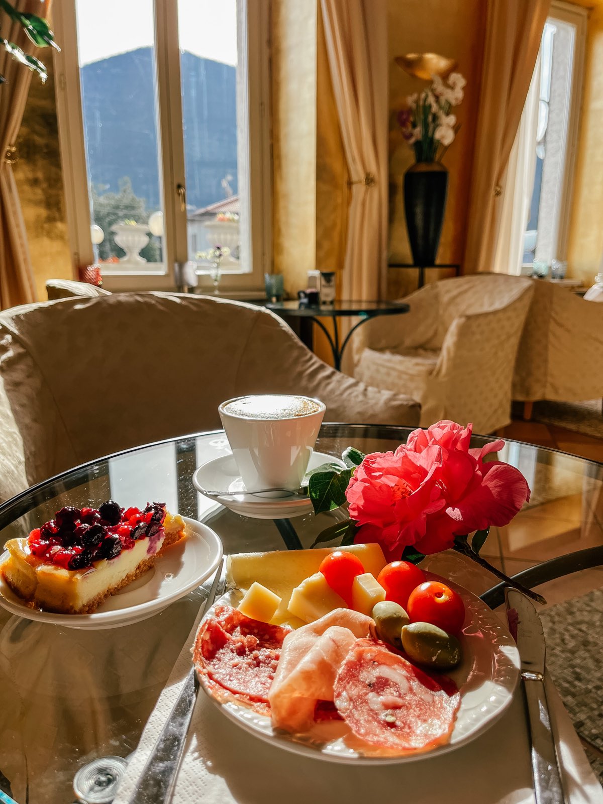 Breakfast in the gold lounge: cake, fruit, a cappuccino and a pink flower.