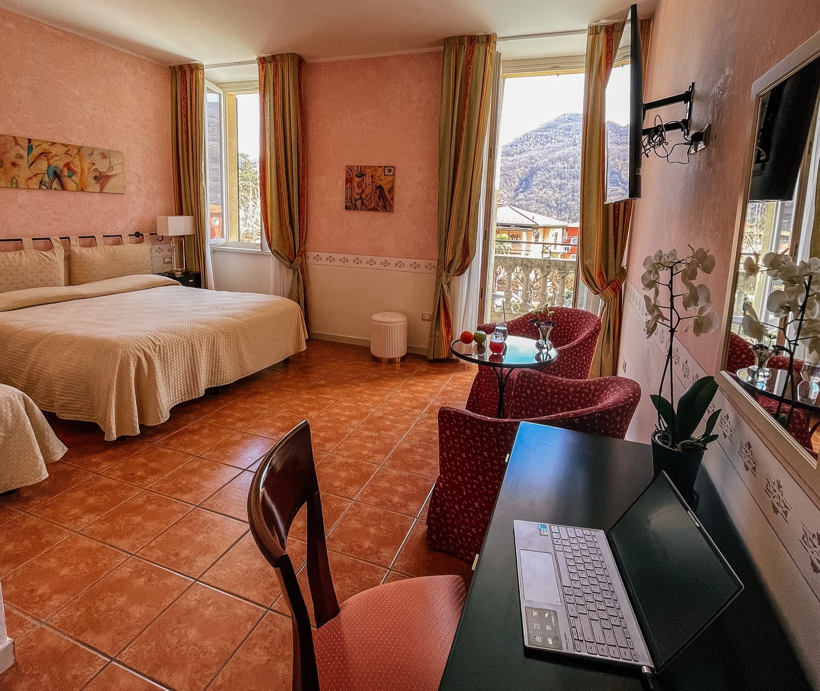 A pink room with a desk and a laptop beside the double bed.
