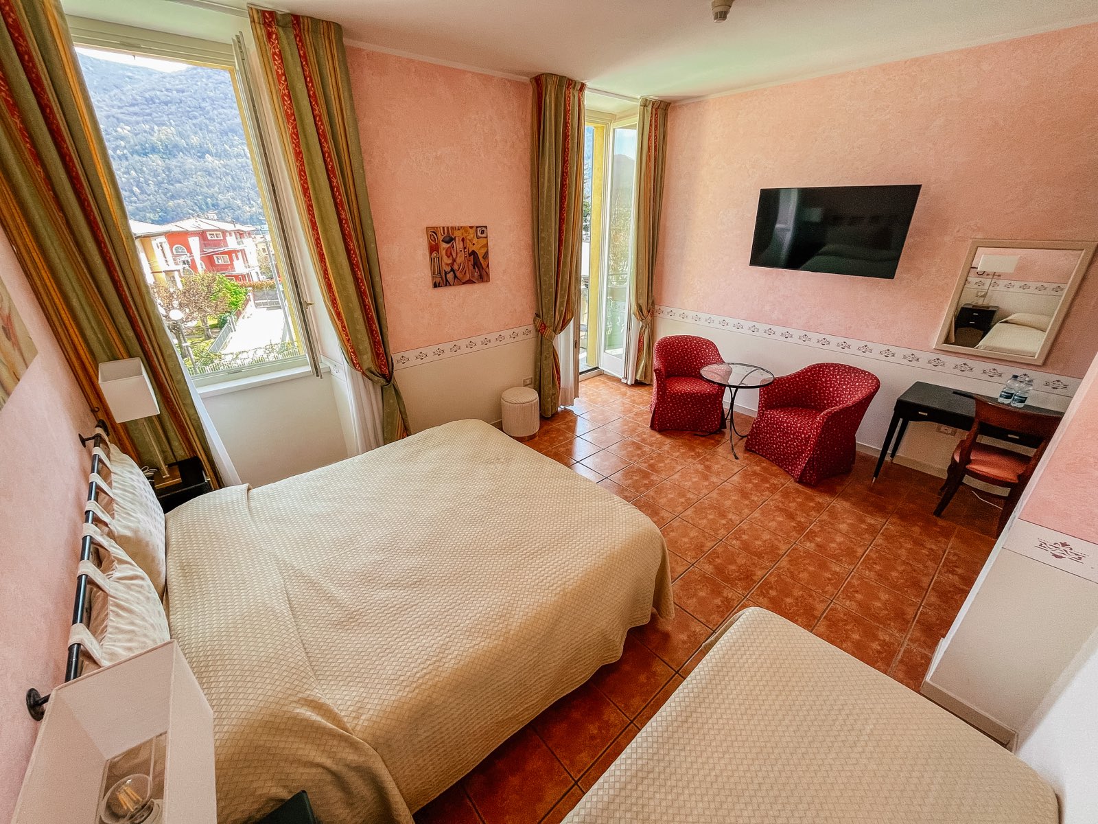 A pink room with a double bed and red armchairs.